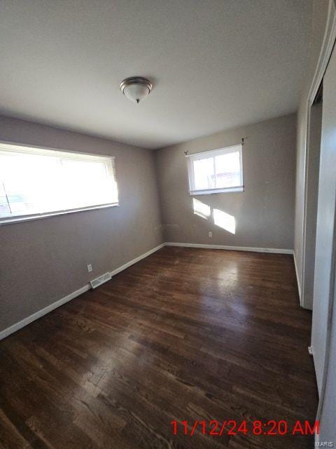 empty room with wood finished floors, visible vents, and baseboards