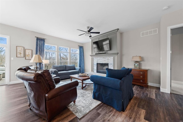 living room featuring ceiling fan, a healthy amount of sunlight, dark hardwood / wood-style flooring, and a stone fireplace