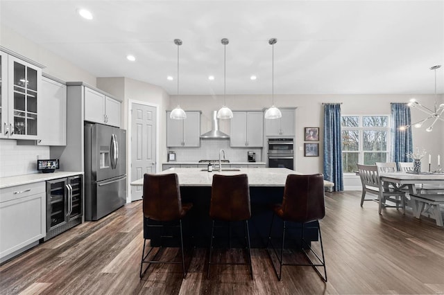 kitchen with wall chimney range hood, decorative light fixtures, stainless steel appliances, and beverage cooler