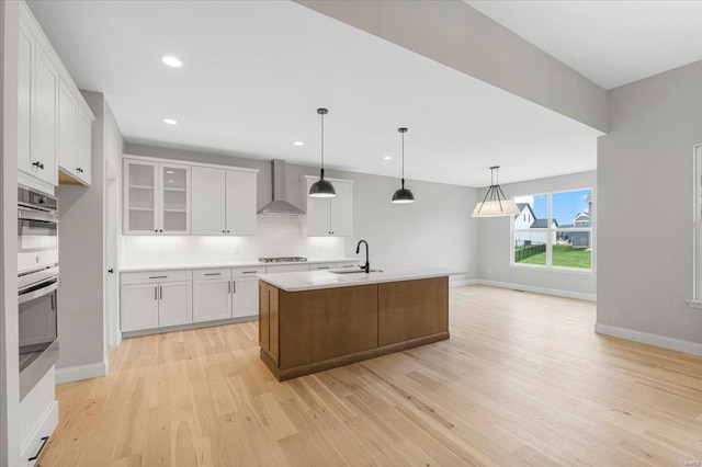 kitchen with wall chimney range hood, a sink, light wood-style floors, stovetop, and white cabinets