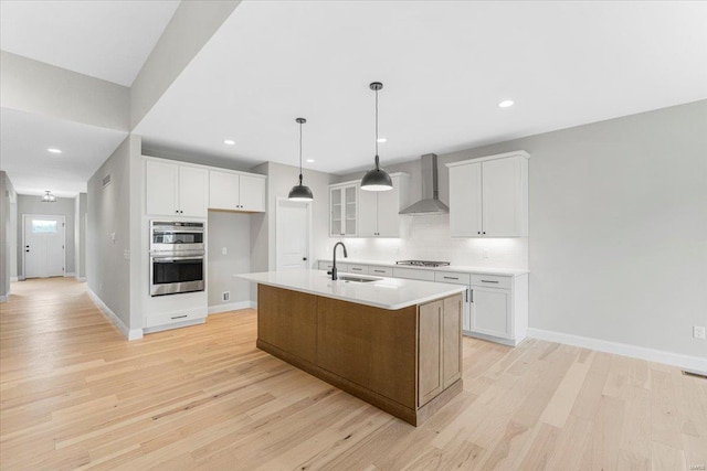 kitchen with light wood-style flooring, a sink, tasteful backsplash, stainless steel double oven, and wall chimney range hood