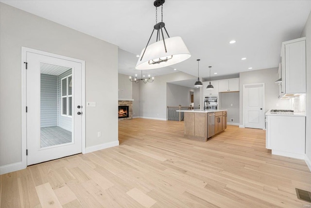 kitchen with white cabinets, light wood-style flooring, a center island with sink, open floor plan, and visible vents