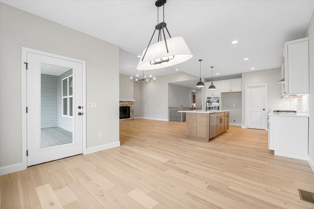 kitchen with light wood finished floors, a kitchen island with sink, open floor plan, visible vents, and white cabinetry