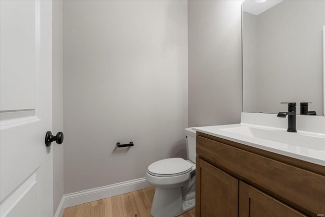 bathroom featuring toilet, vanity, wood finished floors, and baseboards
