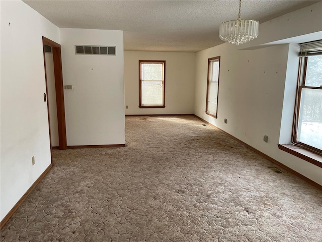 carpeted empty room featuring a notable chandelier and a textured ceiling