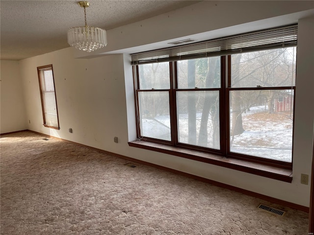 carpeted empty room with a textured ceiling and a notable chandelier