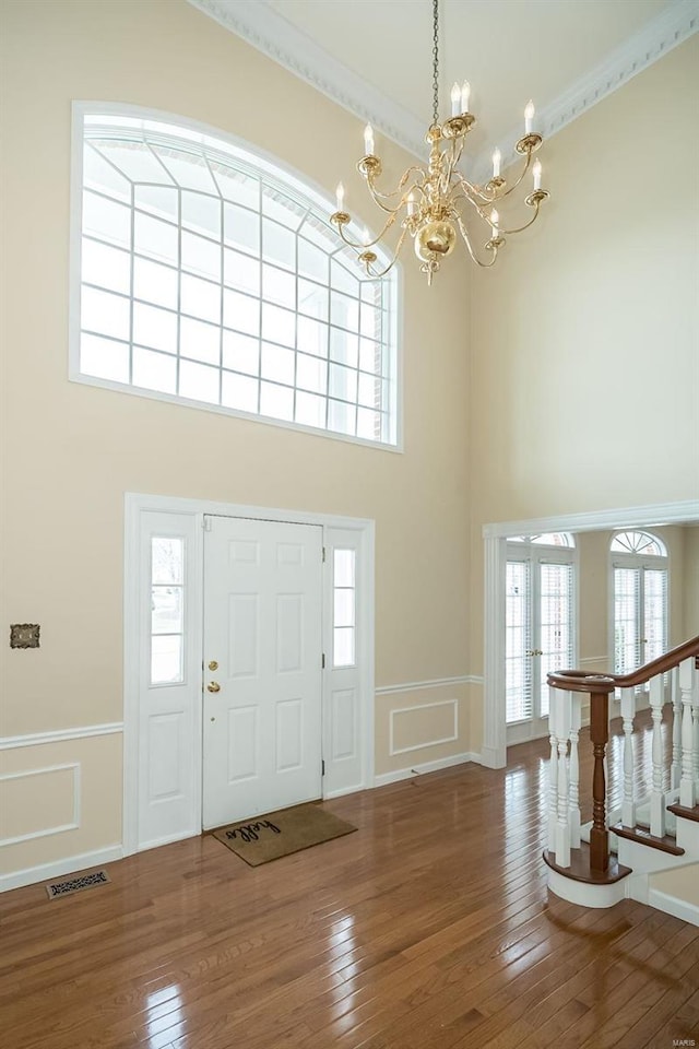 foyer featuring hardwood / wood-style flooring, a notable chandelier, ornamental molding, and a high ceiling