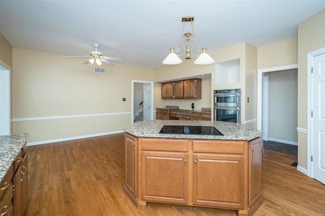 kitchen featuring black electric cooktop, a center island, double oven, and hanging light fixtures