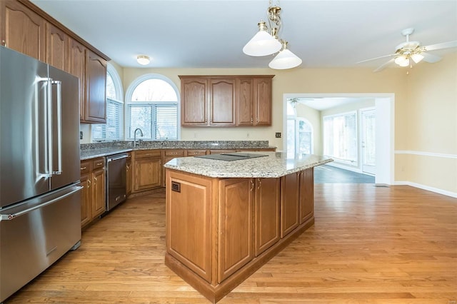 kitchen featuring pendant lighting, light hardwood / wood-style flooring, appliances with stainless steel finishes, a center island, and light stone countertops