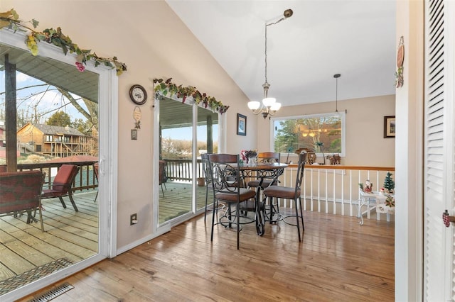 dining room with plenty of natural light, wood-type flooring, vaulted ceiling, and a notable chandelier