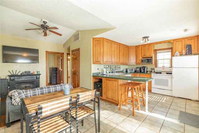 kitchen with a breakfast bar, ceiling fan, light tile patterned floors, white appliances, and vaulted ceiling