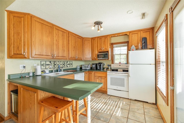 kitchen featuring sink, kitchen peninsula, a textured ceiling, light tile patterned floors, and white appliances