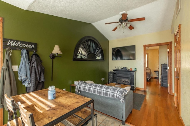 living room with lofted ceiling, wood-type flooring, ceiling fan, and a textured ceiling