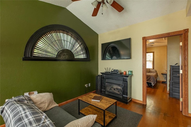 living room with vaulted ceiling, a textured ceiling, dark hardwood / wood-style floors, ceiling fan, and a fireplace