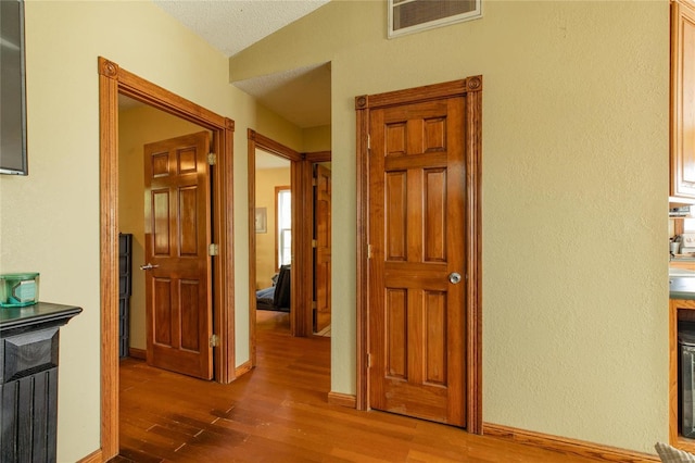 corridor featuring lofted ceiling, hardwood / wood-style floors, and a textured ceiling