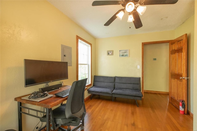 home office with a textured ceiling, electric panel, light hardwood / wood-style flooring, and ceiling fan