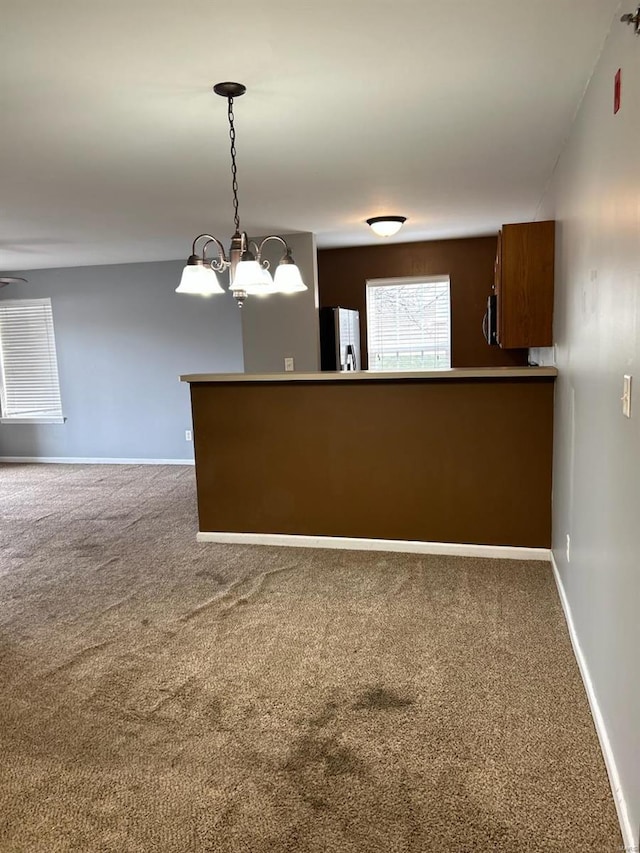 interior space featuring kitchen peninsula, decorative light fixtures, a notable chandelier, carpet floors, and stainless steel refrigerator