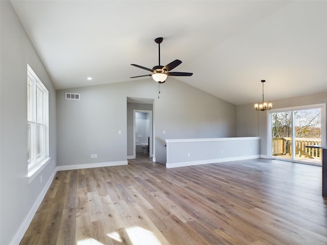 unfurnished living room featuring ceiling fan with notable chandelier, light hardwood / wood-style floors, and vaulted ceiling