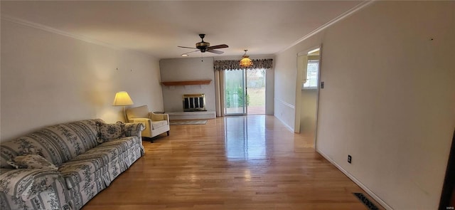 living room with ceiling fan, a large fireplace, ornamental molding, and light wood-type flooring