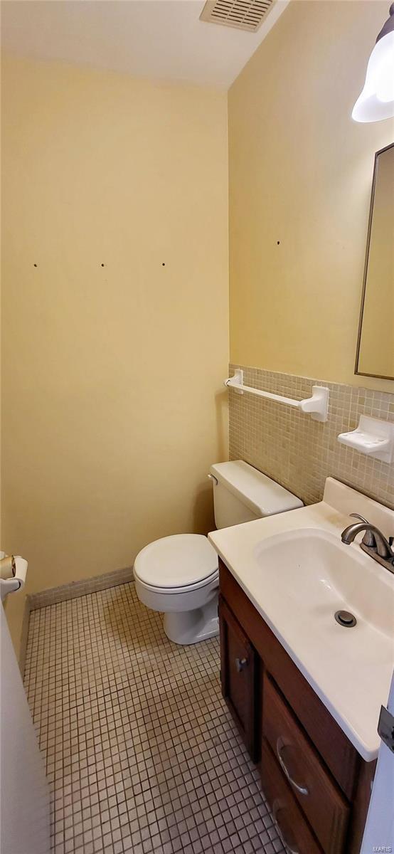 bathroom with toilet, vanity, tile patterned floors, and tile walls