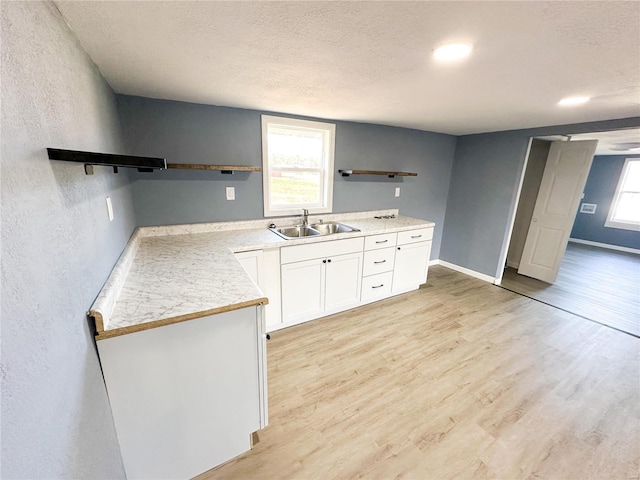 kitchen with white cabinets, a textured ceiling, light wood-type flooring, and sink