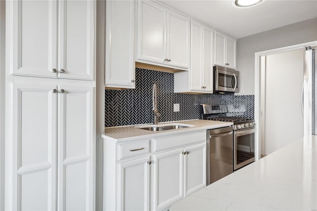 kitchen with light stone countertops, backsplash, stainless steel appliances, sink, and white cabinets