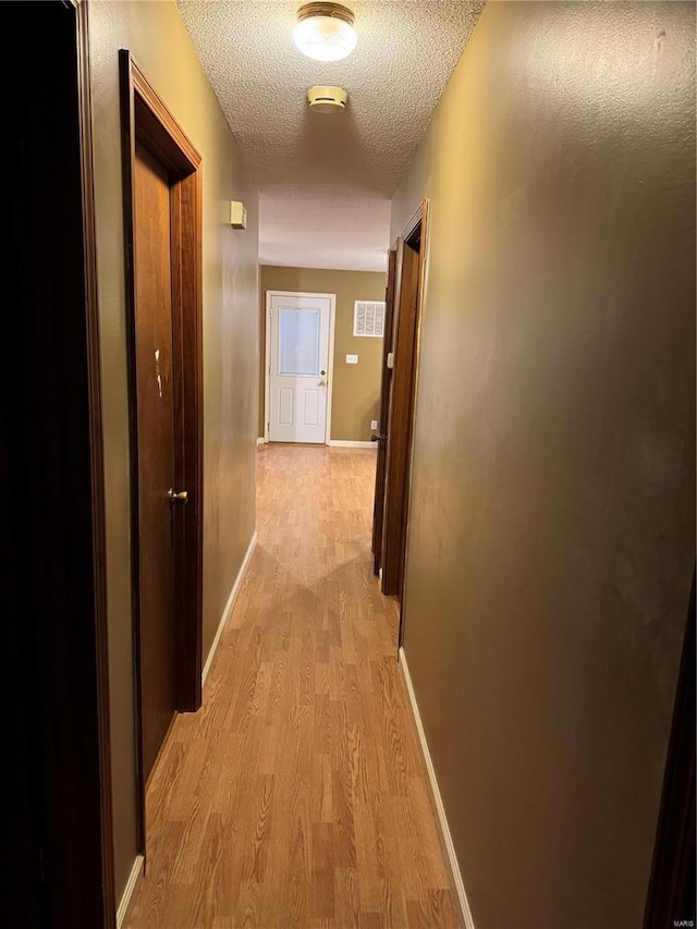 hall with light wood-type flooring and a textured ceiling