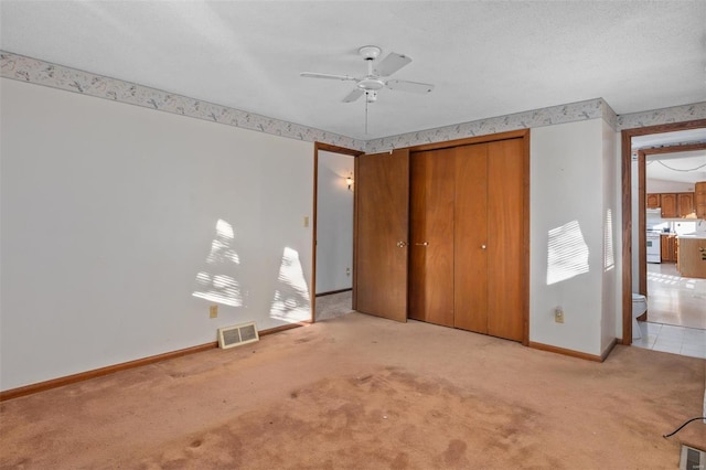 unfurnished bedroom featuring ceiling fan, light colored carpet, a textured ceiling, and a closet