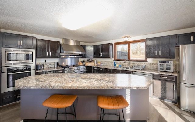 kitchen featuring sink, wall chimney range hood, a kitchen breakfast bar, stainless steel appliances, and a center island