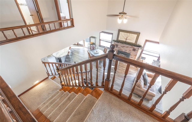 stairway featuring hardwood / wood-style flooring, ceiling fan, a fireplace, and a high ceiling