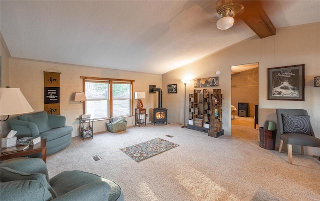 carpeted living room with vaulted ceiling with beams, ceiling fan, a textured ceiling, and a wood stove