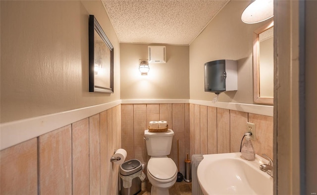 bathroom with sink, wooden walls, a textured ceiling, and toilet