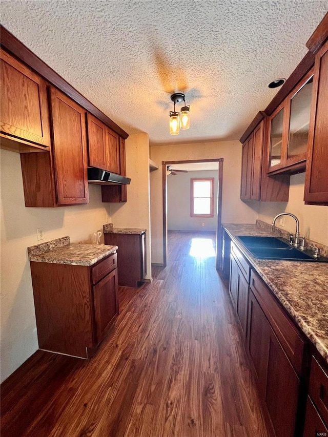 kitchen with a textured ceiling, dark wood-type flooring, sink, and dark stone counters