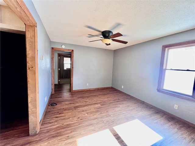 empty room with a textured ceiling, hardwood / wood-style floors, a healthy amount of sunlight, and ceiling fan