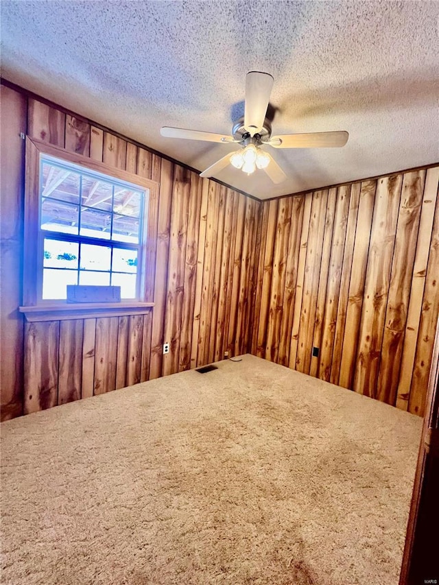 empty room with a textured ceiling, carpet, wooden walls, and ceiling fan