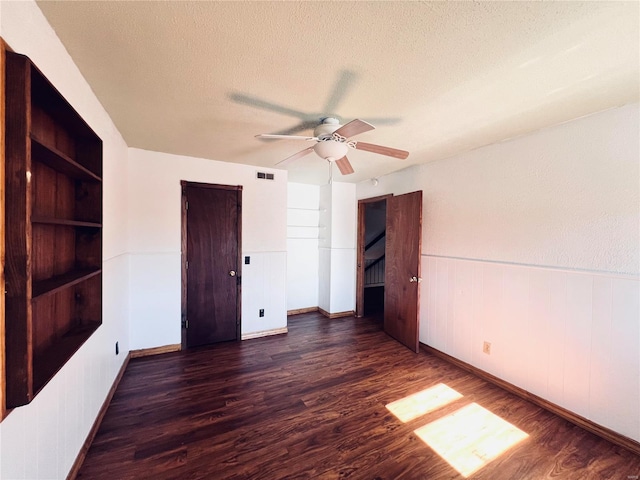 interior space featuring a textured ceiling, built in shelves, dark hardwood / wood-style floors, and ceiling fan