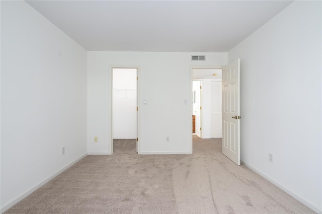 unfurnished bedroom featuring a spacious closet, a closet, and light colored carpet