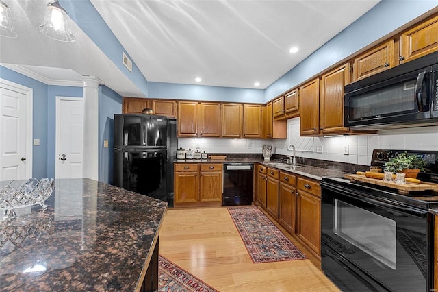 kitchen with backsplash, decorative columns, sink, black appliances, and light hardwood / wood-style flooring