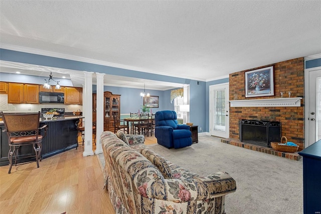 living room with a brick fireplace, a notable chandelier, crown molding, a textured ceiling, and light wood-type flooring