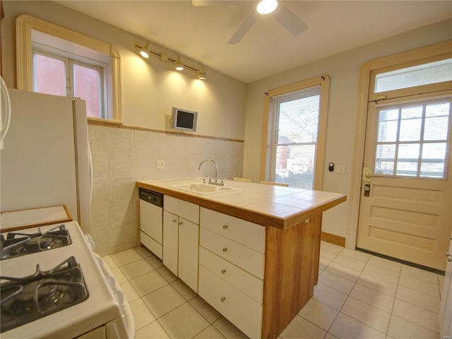 kitchen with tile counters, sink, white appliances, light tile patterned flooring, and tile walls