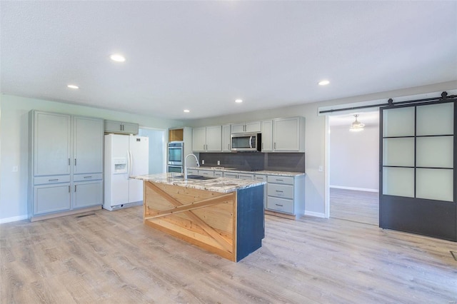 kitchen featuring light stone counters, stainless steel appliances, sink, a barn door, and gray cabinets