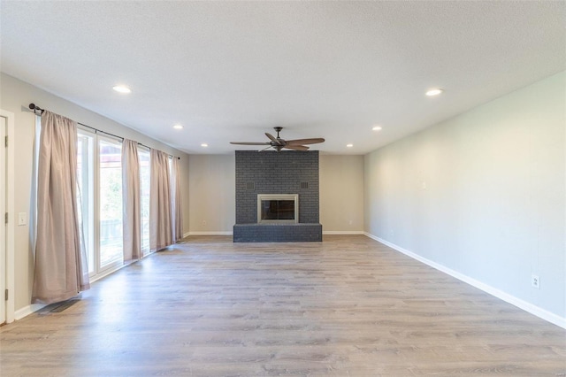 unfurnished living room featuring a brick fireplace, a textured ceiling, light hardwood / wood-style flooring, and ceiling fan