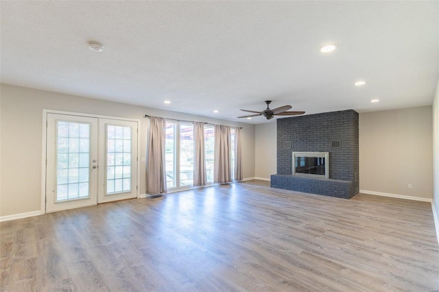 unfurnished living room with french doors, a brick fireplace, light hardwood / wood-style flooring, ceiling fan, and a textured ceiling