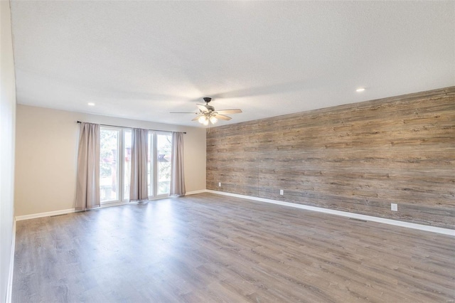 empty room featuring wooden walls, ceiling fan, a textured ceiling, and light wood-type flooring