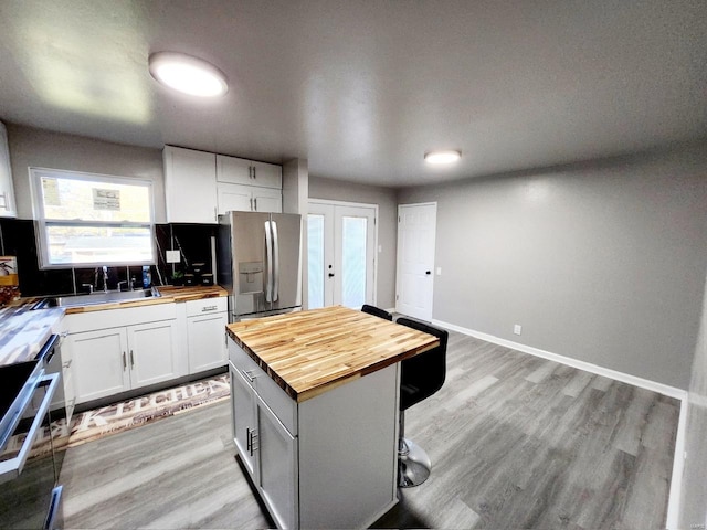 kitchen featuring butcher block counters, white cabinetry, a breakfast bar, appliances with stainless steel finishes, and light wood-type flooring