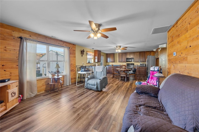 living room with ceiling fan, wood-type flooring, and wood walls