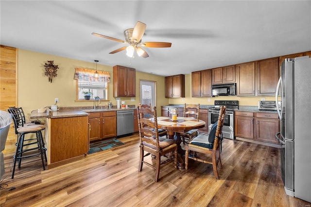 kitchen featuring pendant lighting, light hardwood / wood-style flooring, a breakfast bar, ceiling fan, and stainless steel appliances