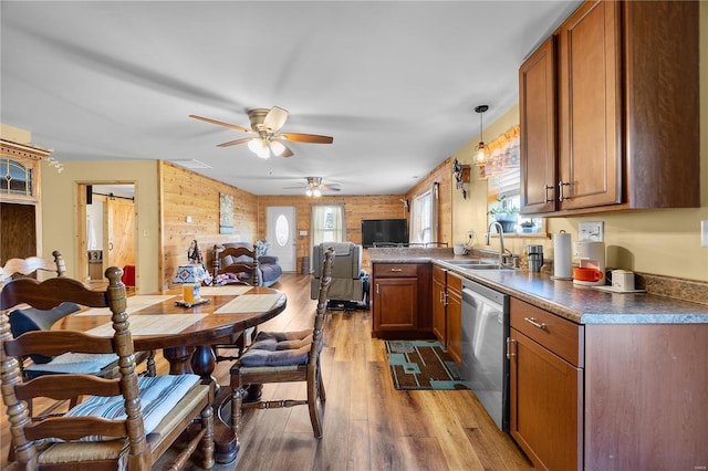 kitchen with sink, wood walls, wood-type flooring, hanging light fixtures, and dishwasher