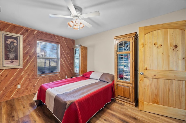 bedroom with hardwood / wood-style flooring, ceiling fan, and wooden walls