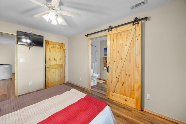 bedroom with a barn door, dark hardwood / wood-style floors, connected bathroom, and ceiling fan